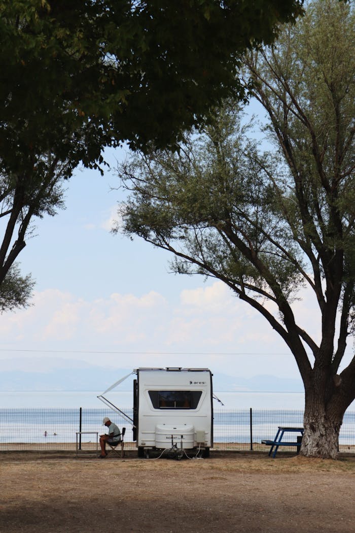 Tranquil scene of a camper by the beach under trees in summer, perfect for travel and recreation themes.